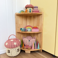 A corner wooden toy shelf styled with pastel wooden toys, including rainbow blocks, cone shapes, a wicker basket house, and a mushroom-shaped basket, next to a yellow cabinet.